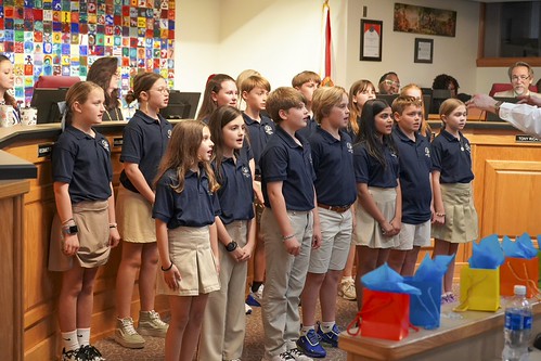 Group of students in matching uniforms singing in a room with wooden benches and a table.