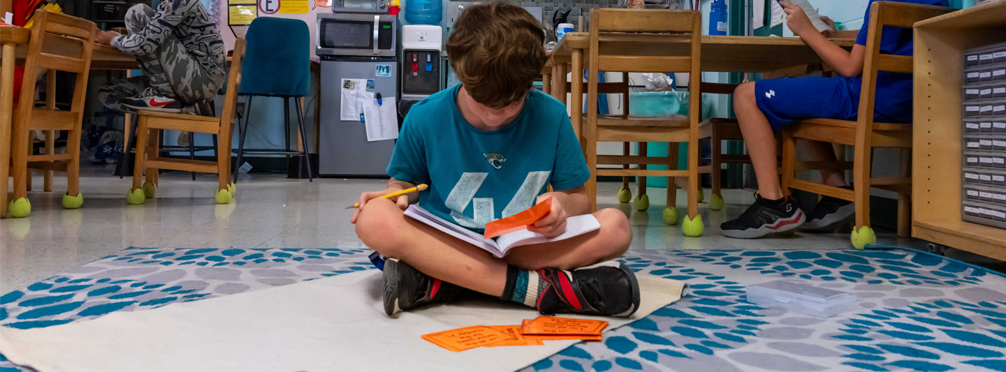 Student sitting cross-legged on classroom floor reading