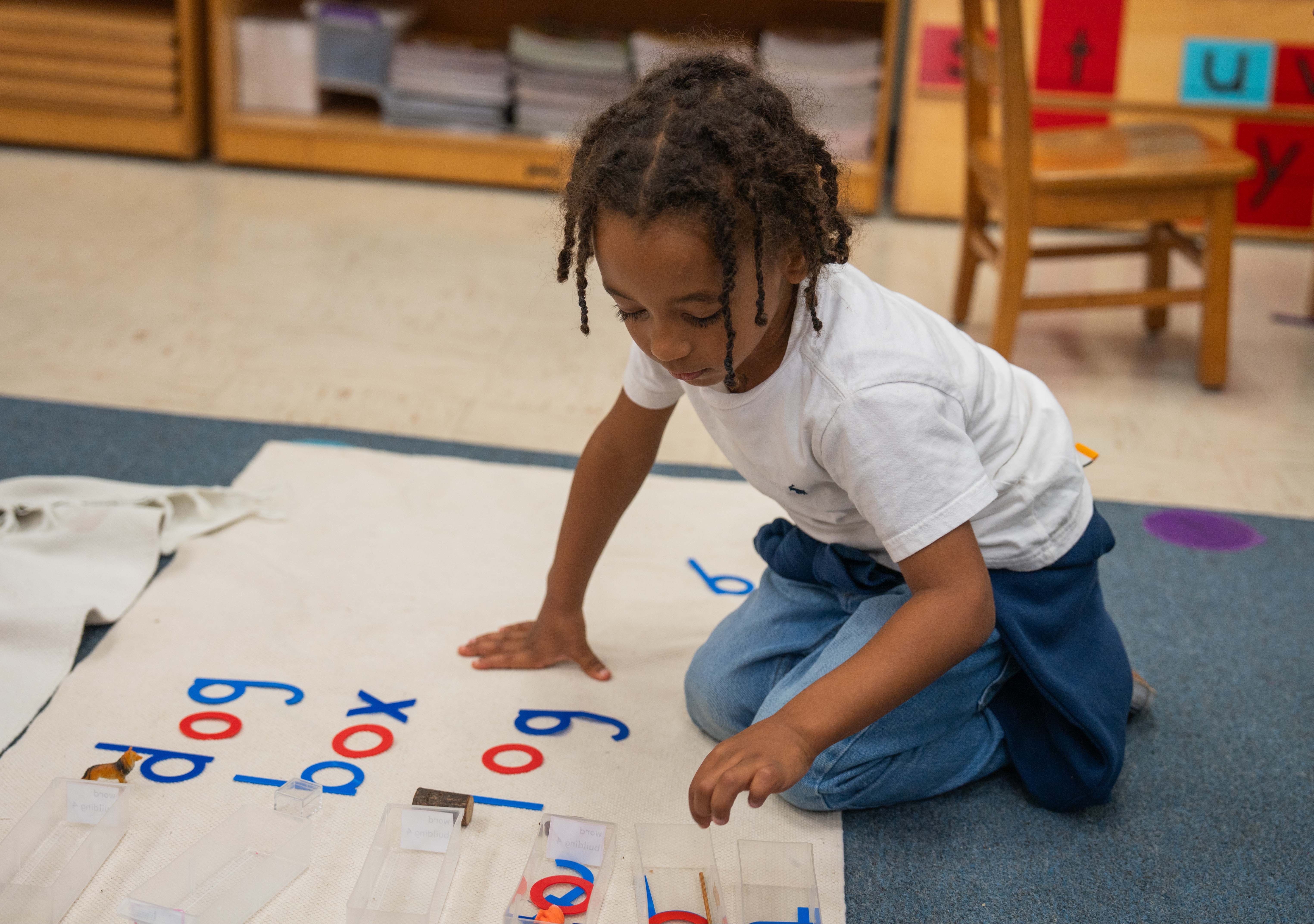 Male student sitting on the floor working with letters and photos.  Building words that match the photos with the letters.