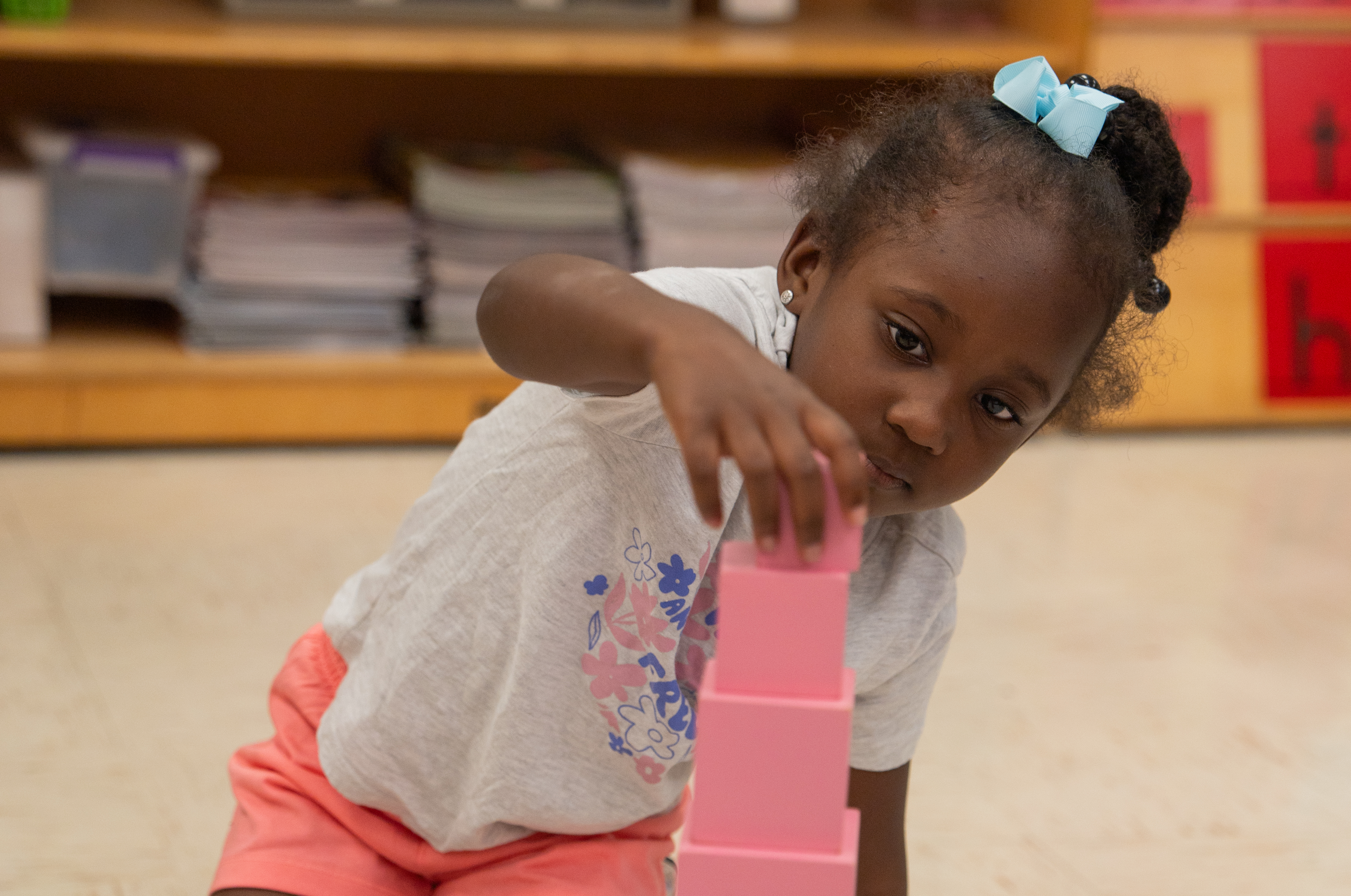 Female student sitting on the ground stacking red blocks by size.