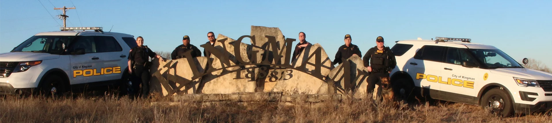 Police officers standing by police cars and Kingman city sign 