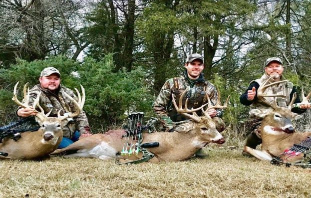 Three hunters in camo holding deer by antlers 