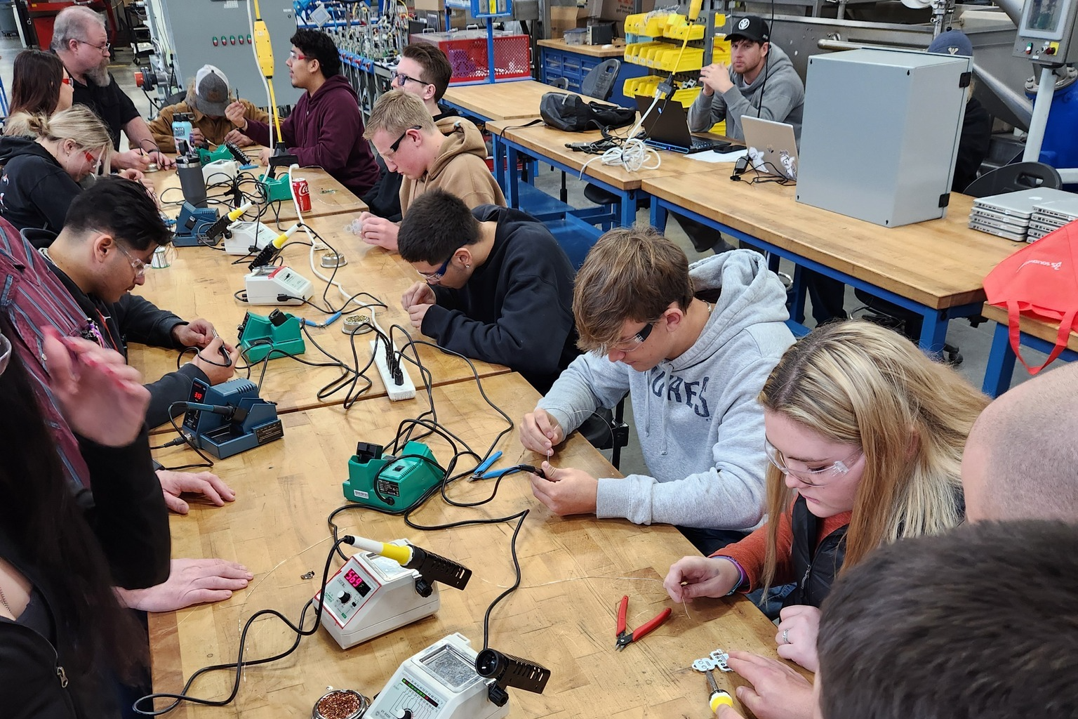 Students work with electronic tools wearing safety goggles.