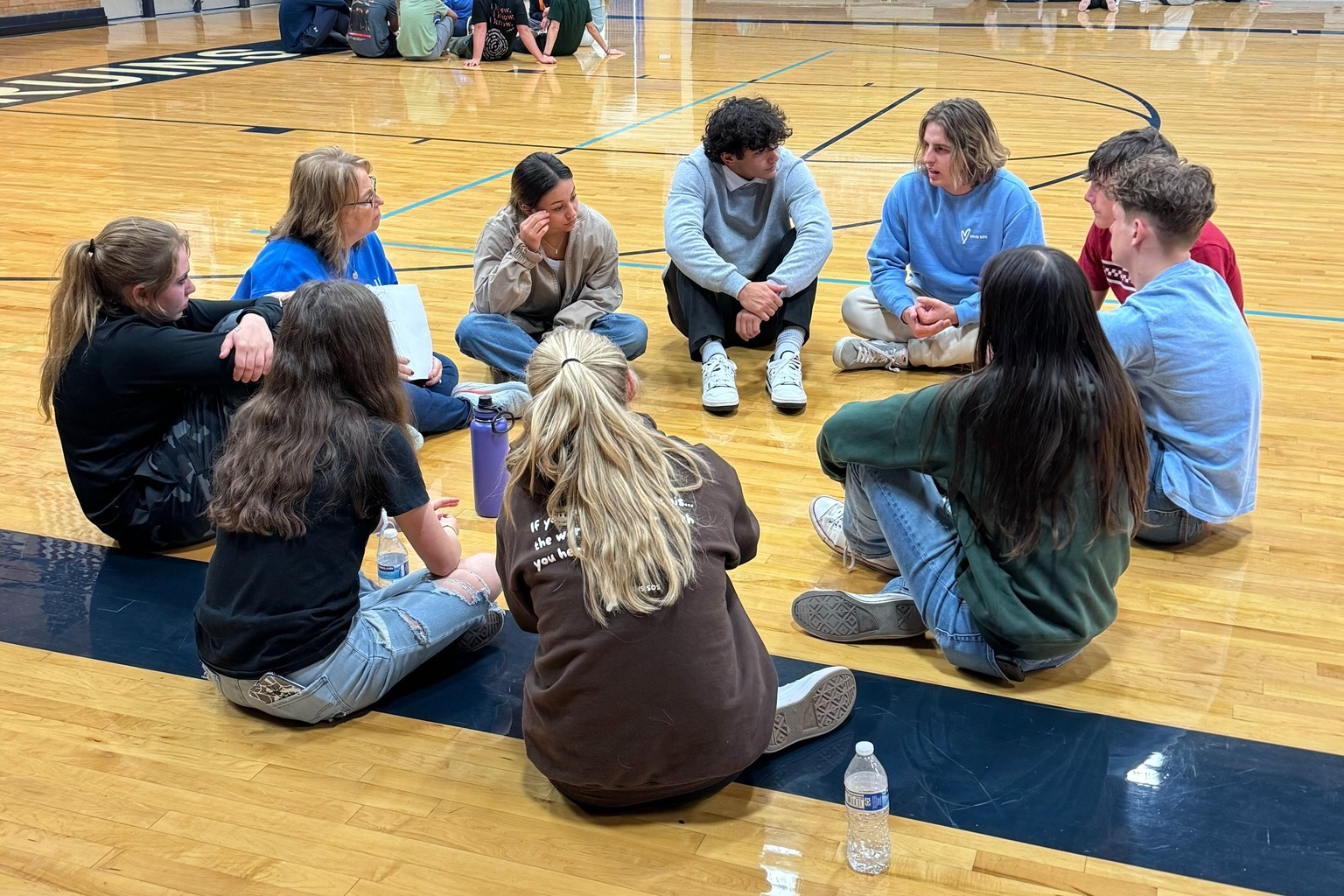 Students sit in a circle on the gym floor.