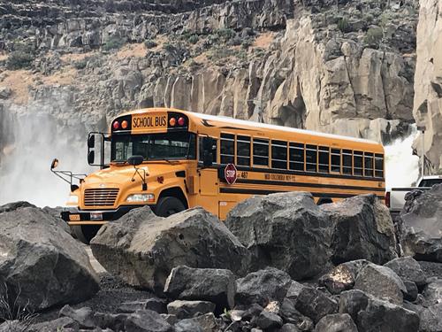 School Buss Parked in frount of a waterfall.