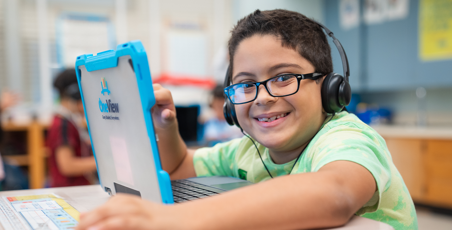 student with headphones smiling while working on a laptop