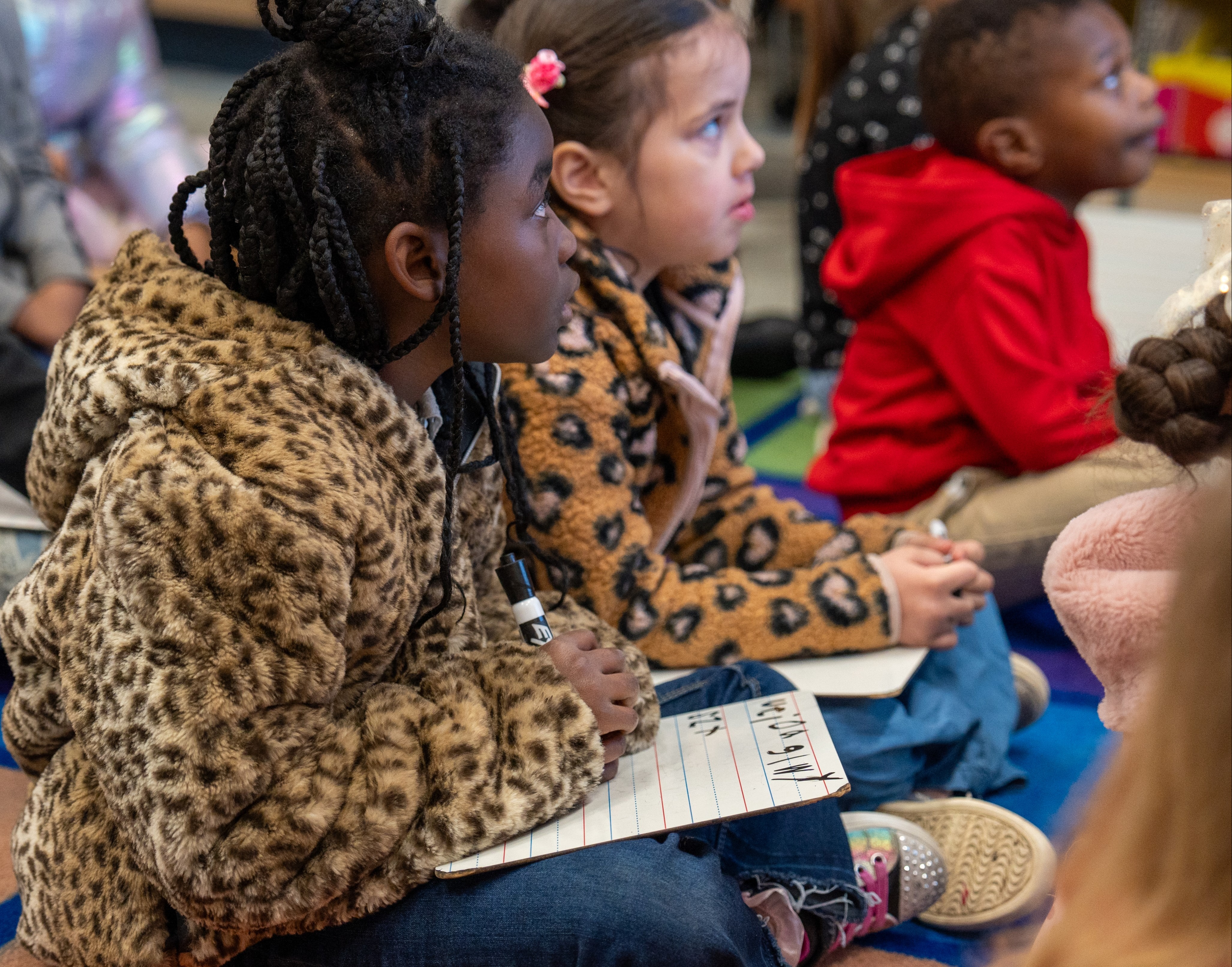 Two students sitting on a carpet with writing boards and black markers