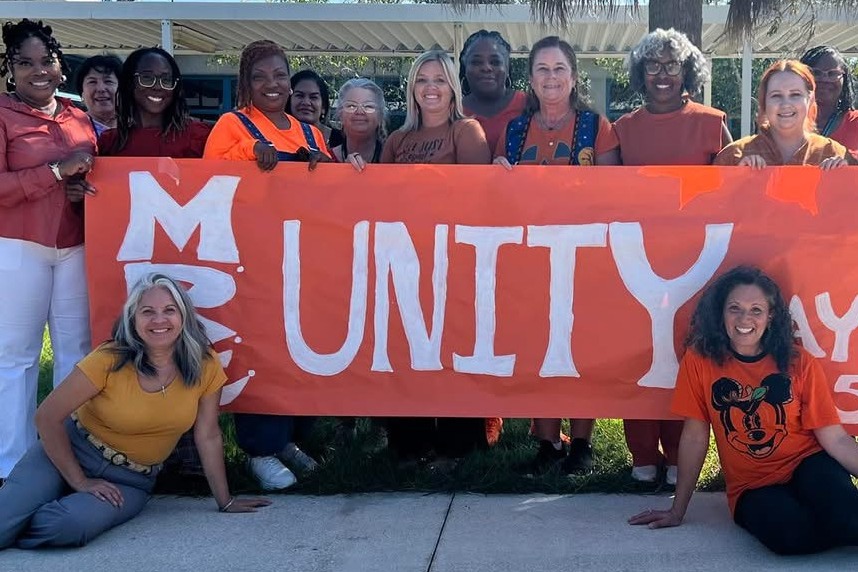 Teachers behind an orange banner that says Unity in white paint