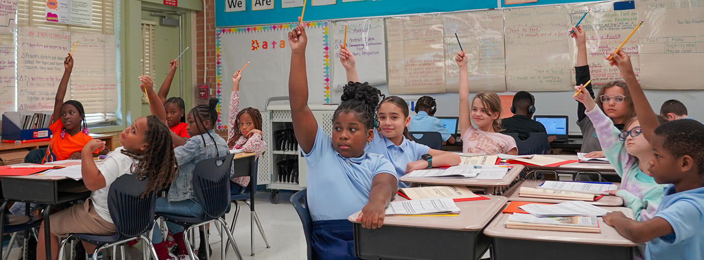 students at their desks raising their hands