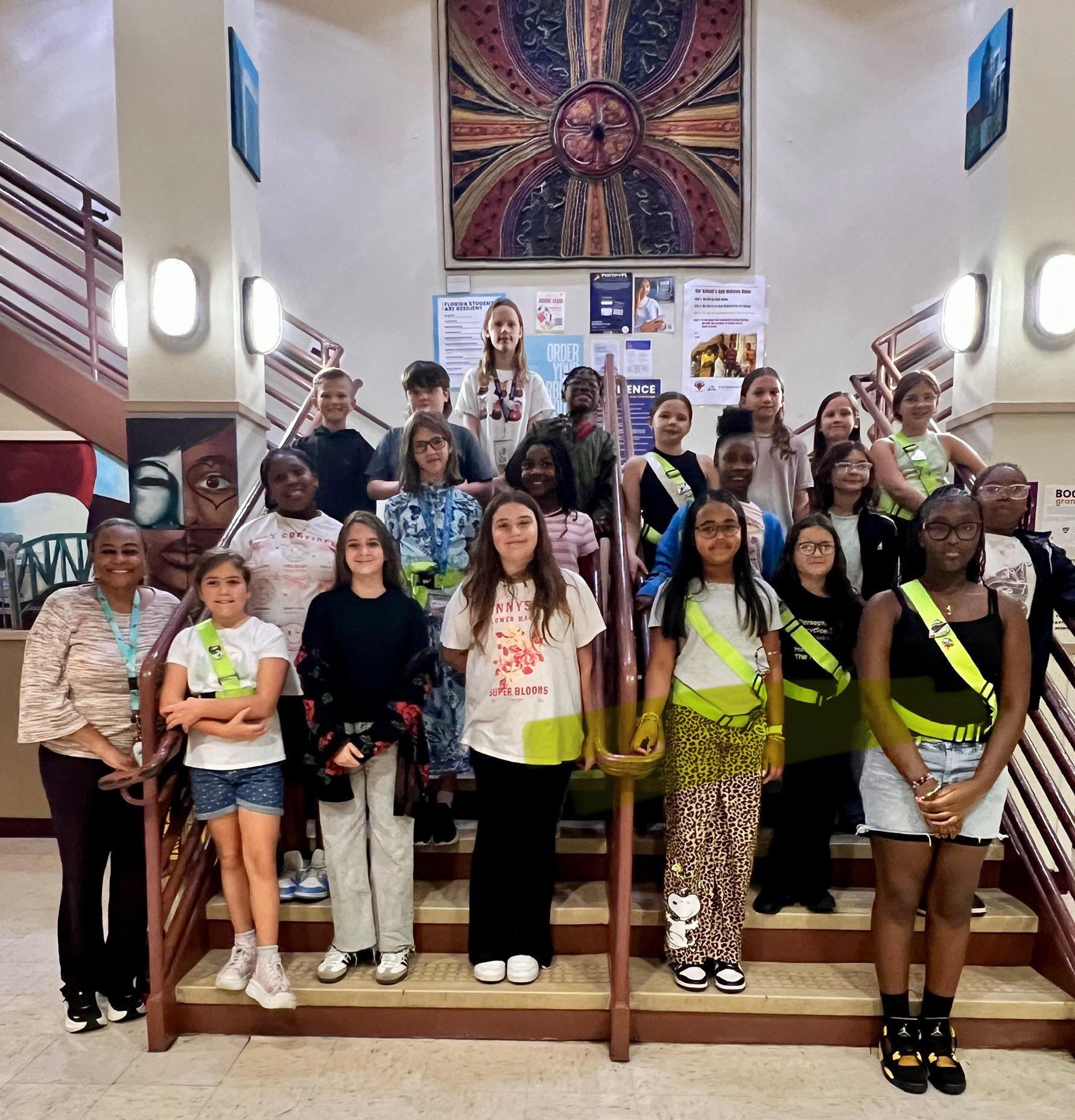 Group of young people, some with sashes, posing for a photo on a staircase with white walls.