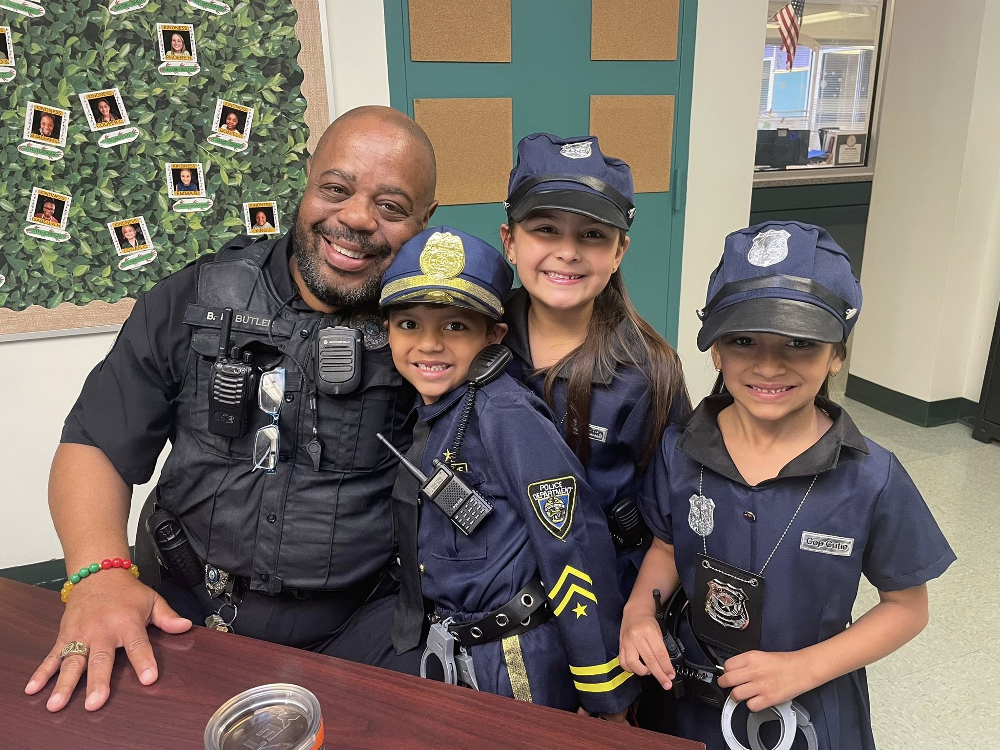 A man in a police uniform poses with three children dressed as police officers, standing behind a table.