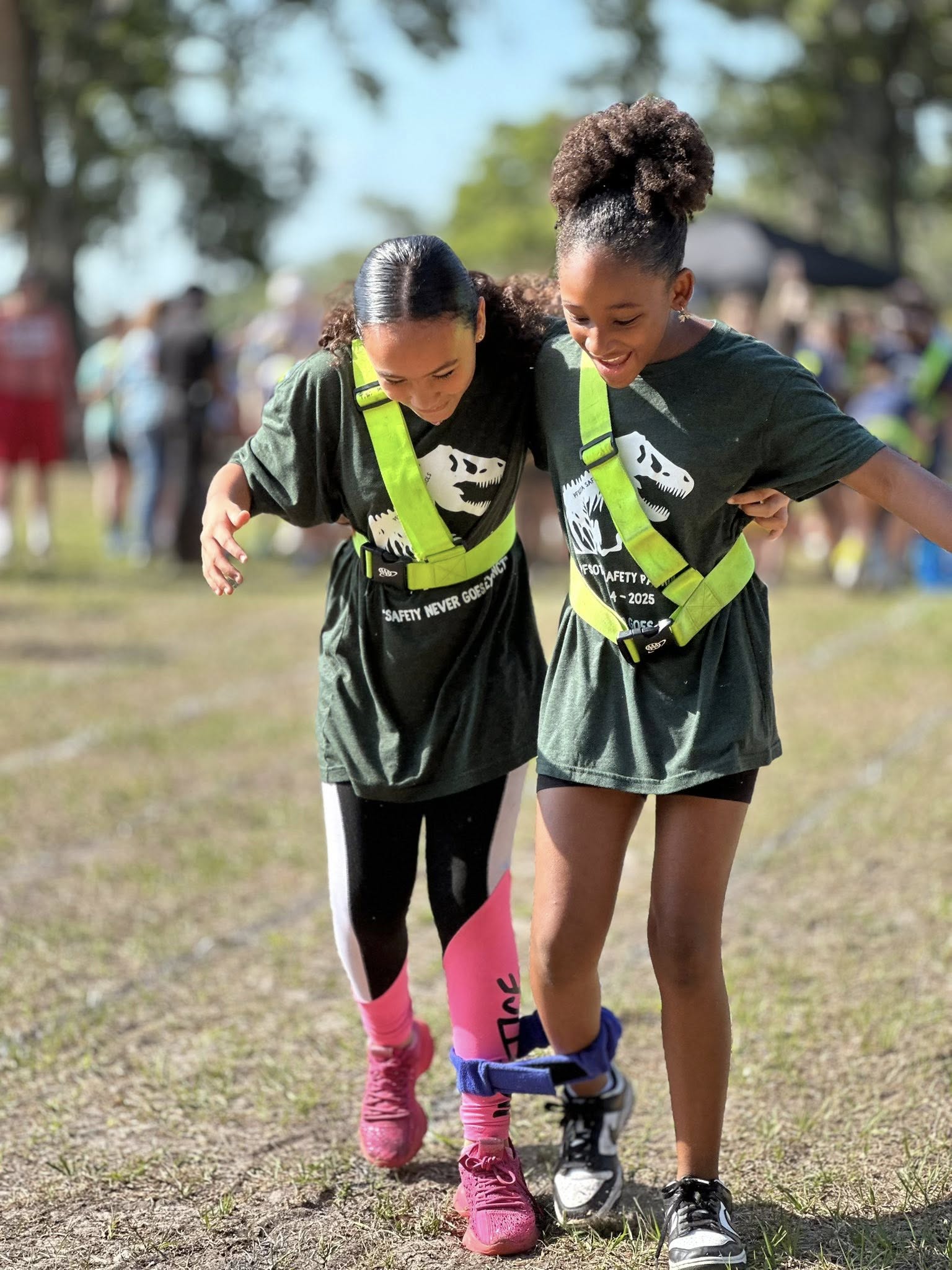 Two students wearing safety patrol belts doing a 3 legged race
