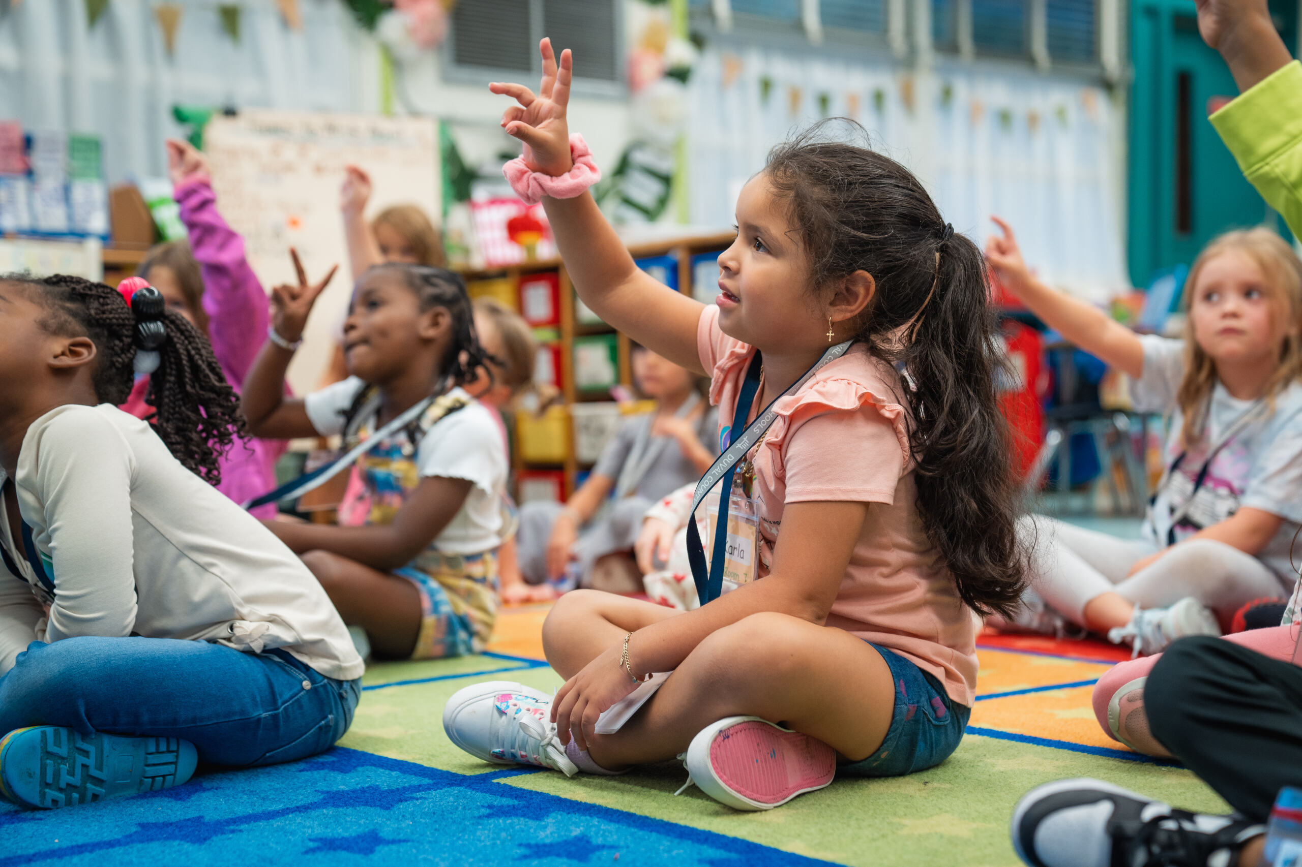 A student on the carpet raising her hand