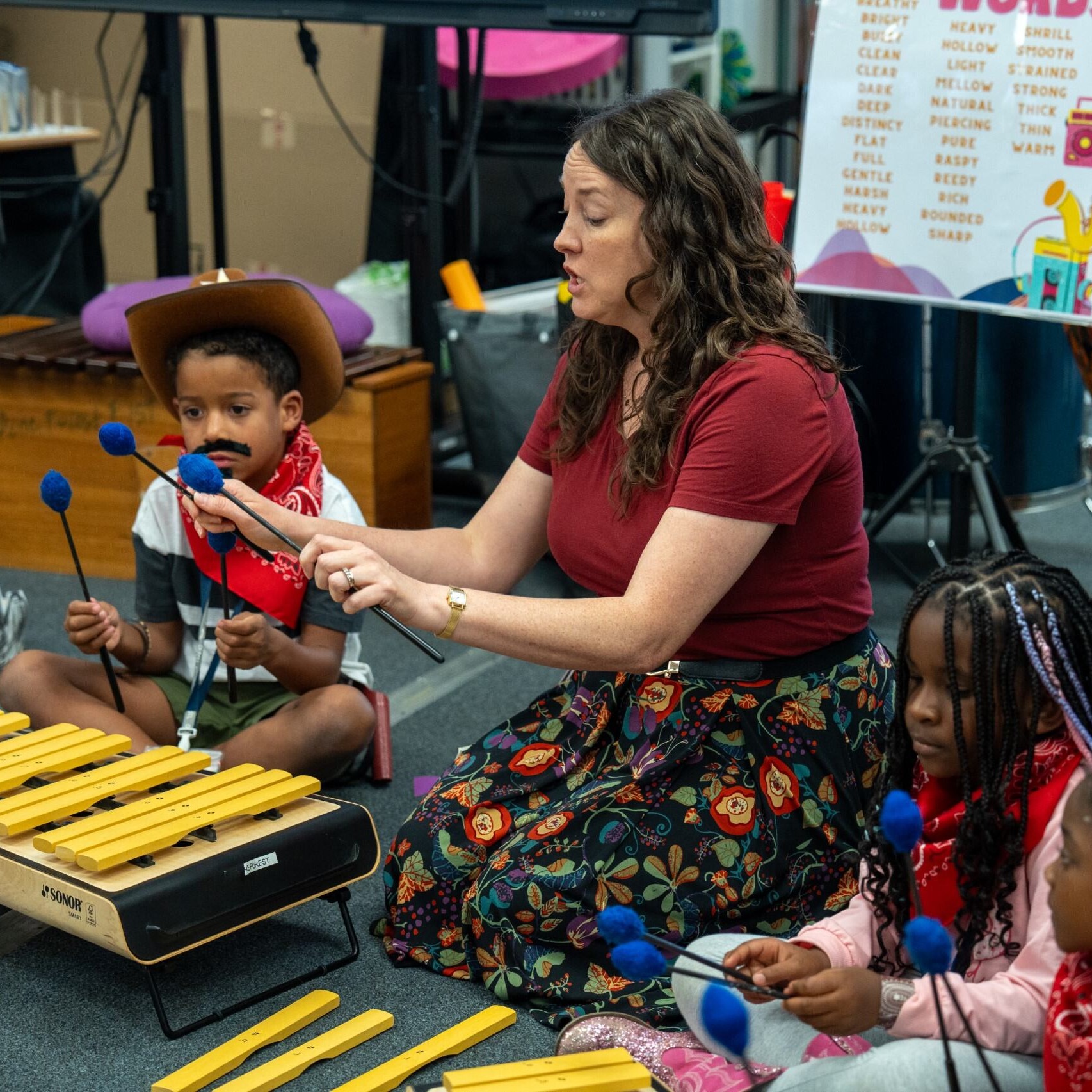 teacher demonstrating how to play an instrument while the class sits in a circle on the carpet