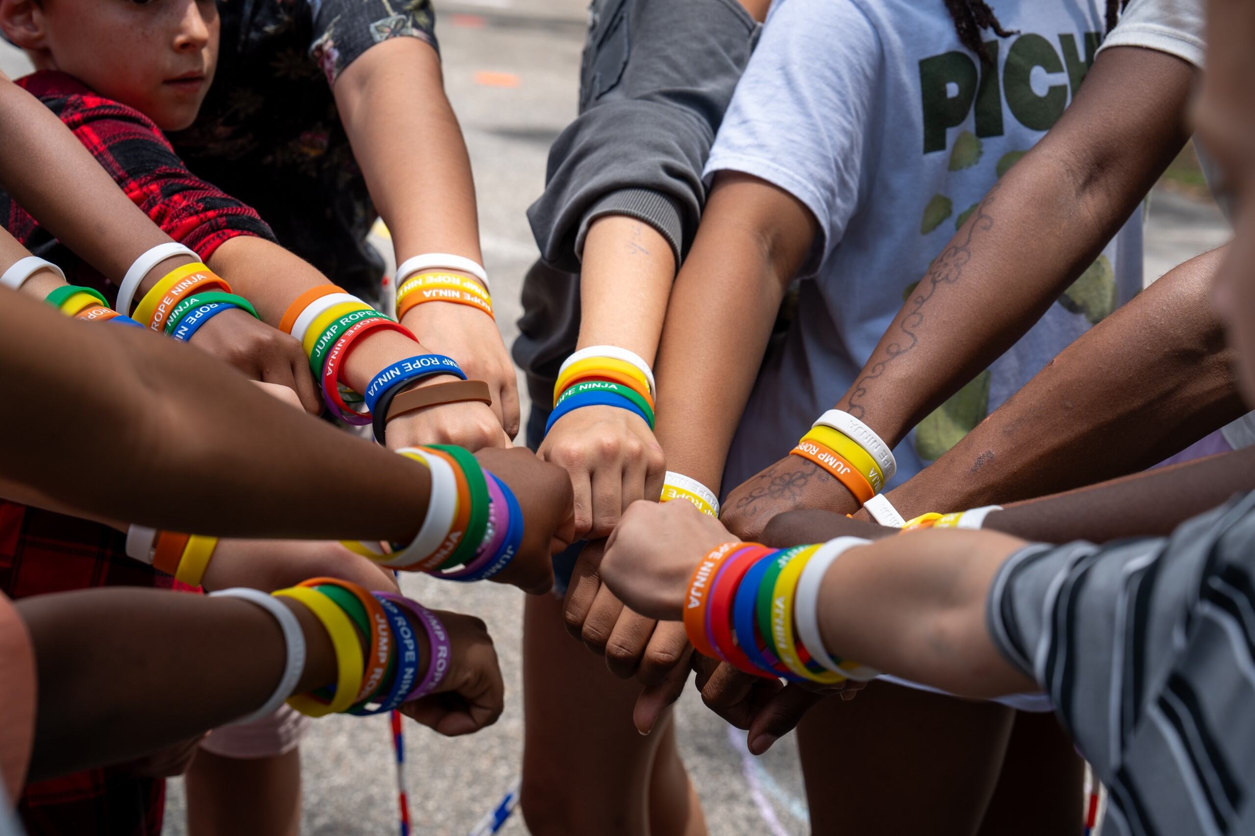 Students with their hands together in a huddle with colorful rubber bracelets on