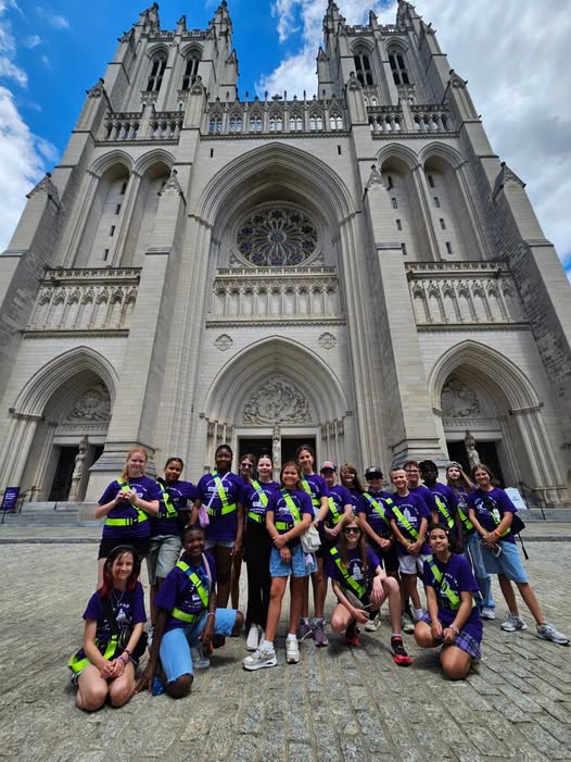 A group of people in matching uniforms stand and crouch in front of a large cathedral.