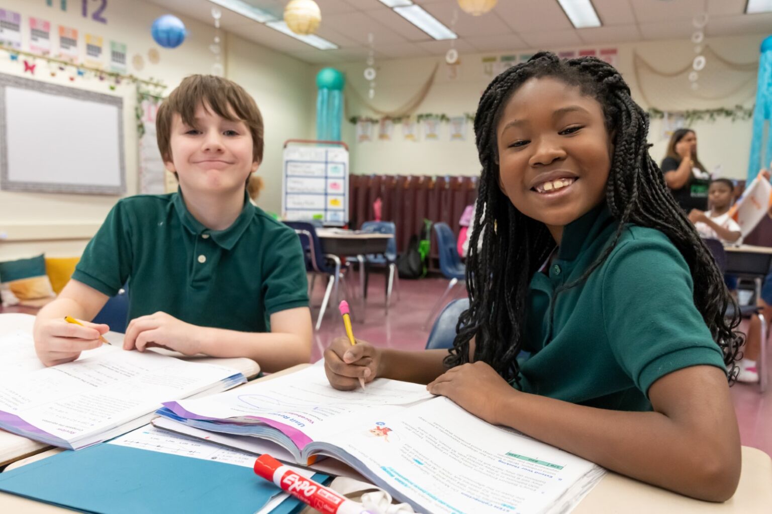 A girl and boy at their desk smiling at the camera