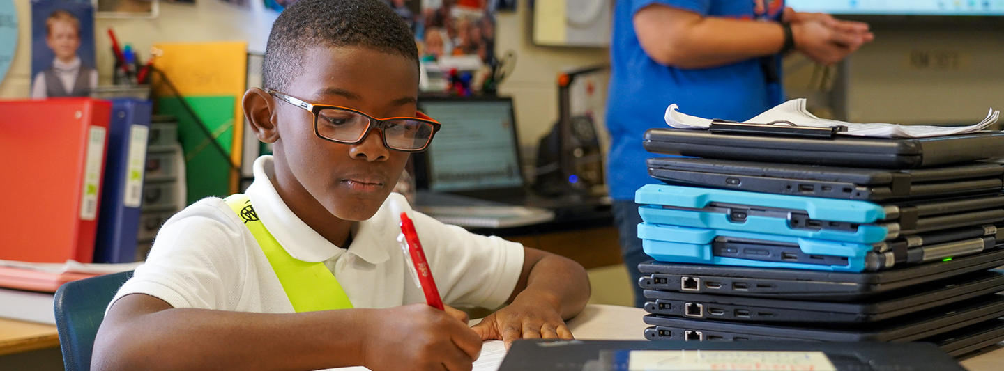 student working on assignment next to a stack of laptops