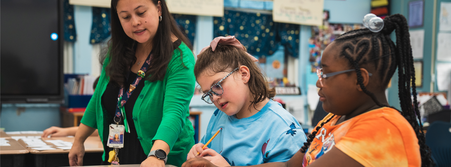 teacher helping two students work on their classwork