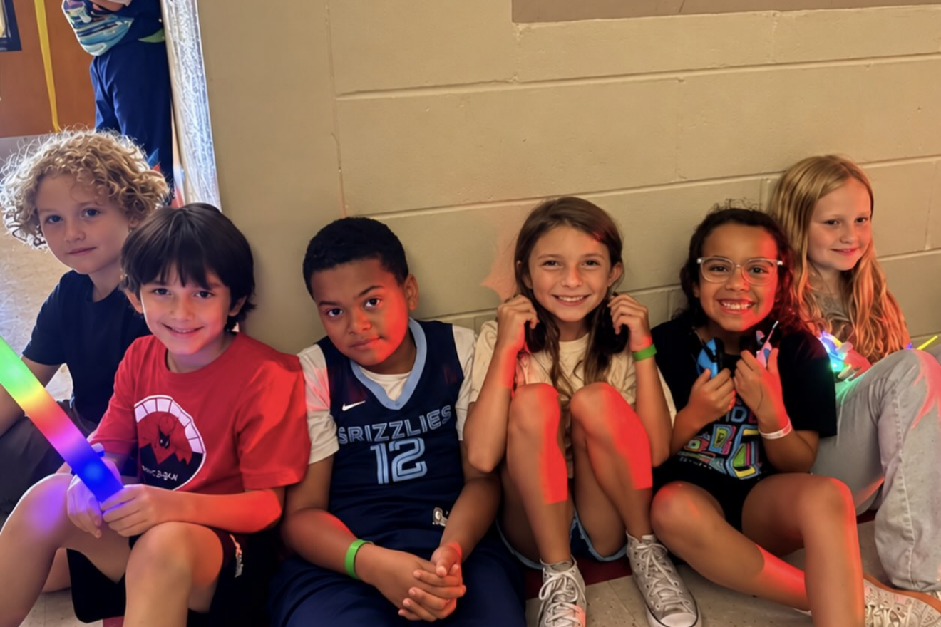 Group of young children sitting on a bench wearing sports jerseys, holding light-up toys.