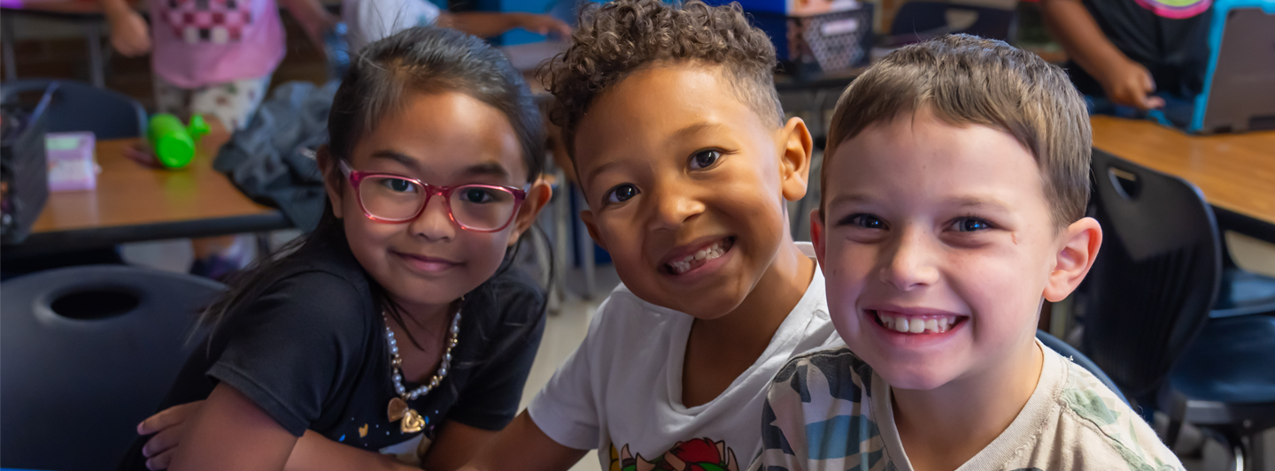 three students in class smiling up at the camera