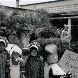 A group of children posing for a photo in front of a school building, with one child holding a sign .