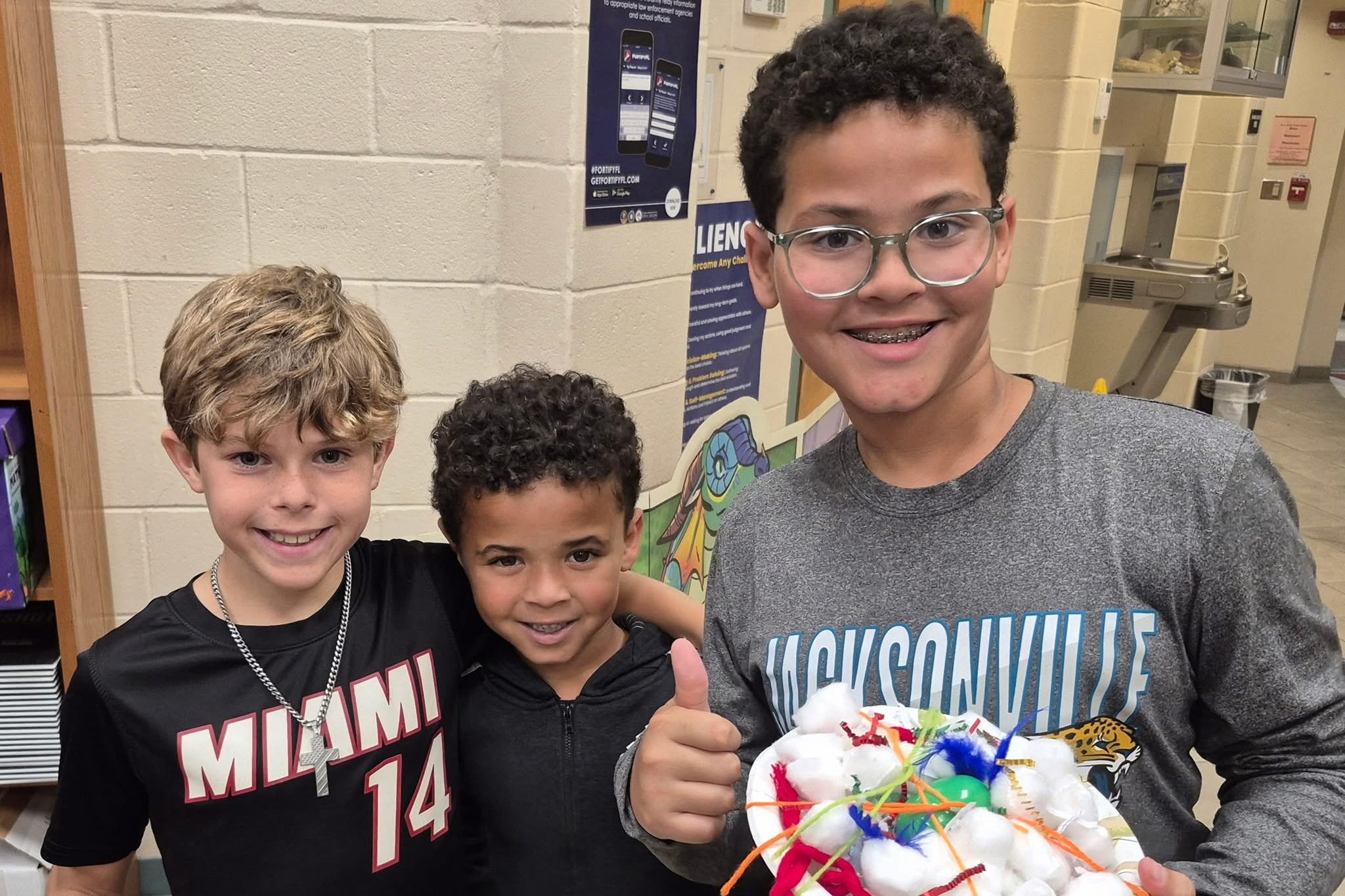 Three kids stand together in a room, holding plates with constructions made of cotton balls.