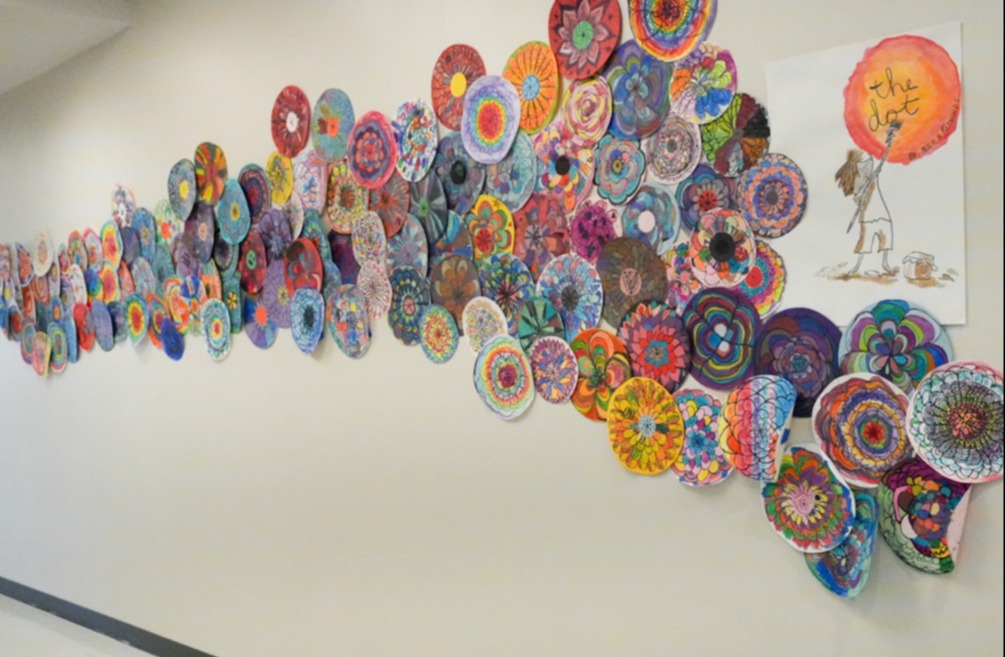 A hallway with a wall displaying a large, colorful art installation made of circular, layered paper cutouts.