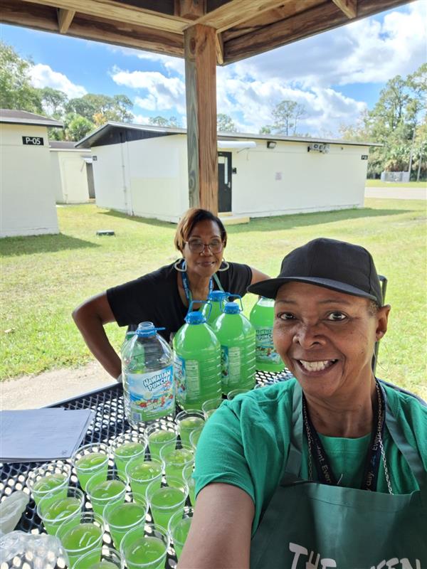 Two people, one standing behind a table laden with drinks and bottles, posing for the camera.