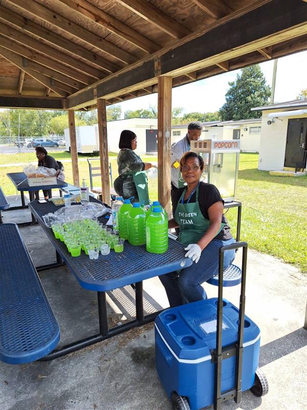 A woman preparing food in an outdoor setting, with various beverages and dining items around her.