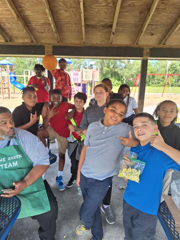 Group of children gathered under pavilion, posing for photo with their teacher.