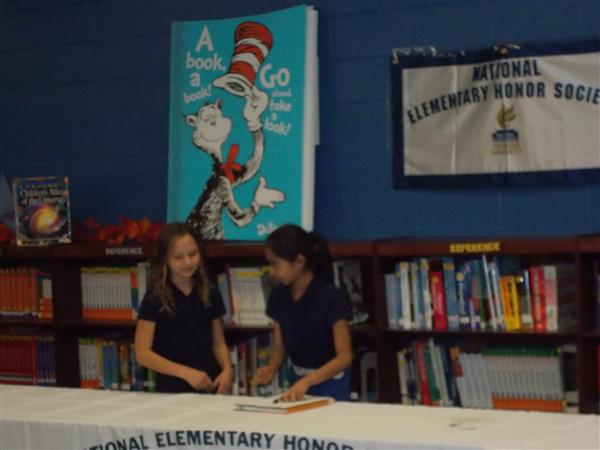 Two girls at a book display, one girl is holding an orange ribbon.