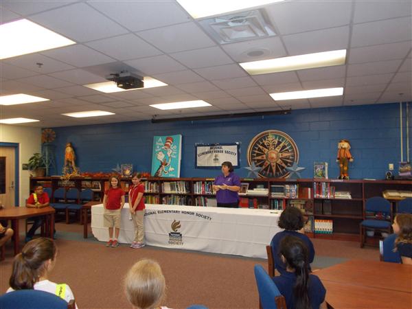 People standing in front of a table with an award on it, in a room with a bookshelf and a poster.