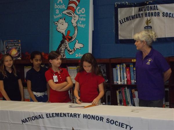 A group of people in a library, with one person signing a document.