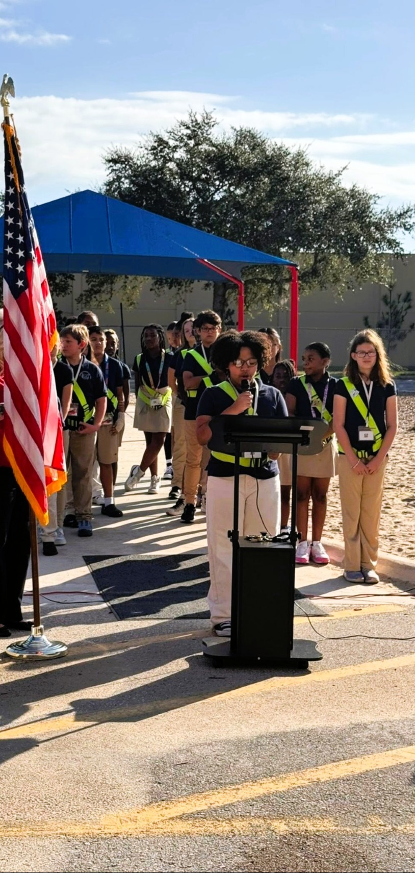 A group of students wearing matching uniforms and lanyards stand in a row at a school event.