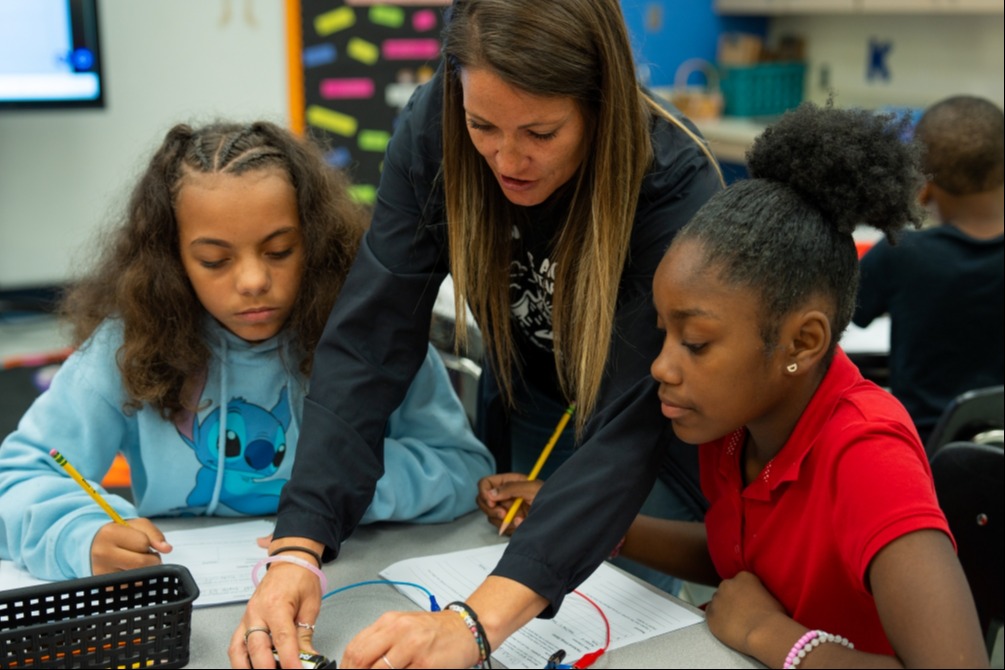 A woman and two girls sit at a table, working on a project together in a classroom.