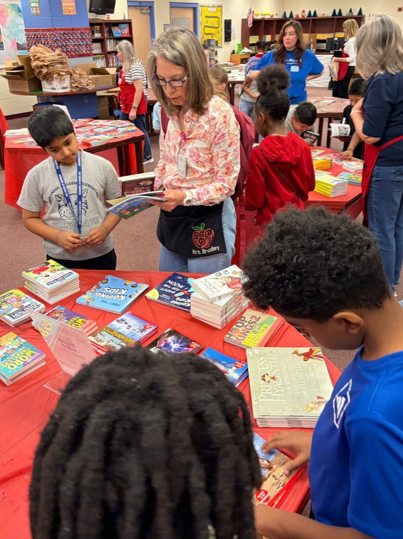 Indoor area with tables and chairs. Children and adults are gathered around a table filled with books.