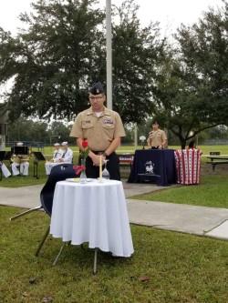 veteran soldier in uniform, standing at attention beside a table with a candle on it.
