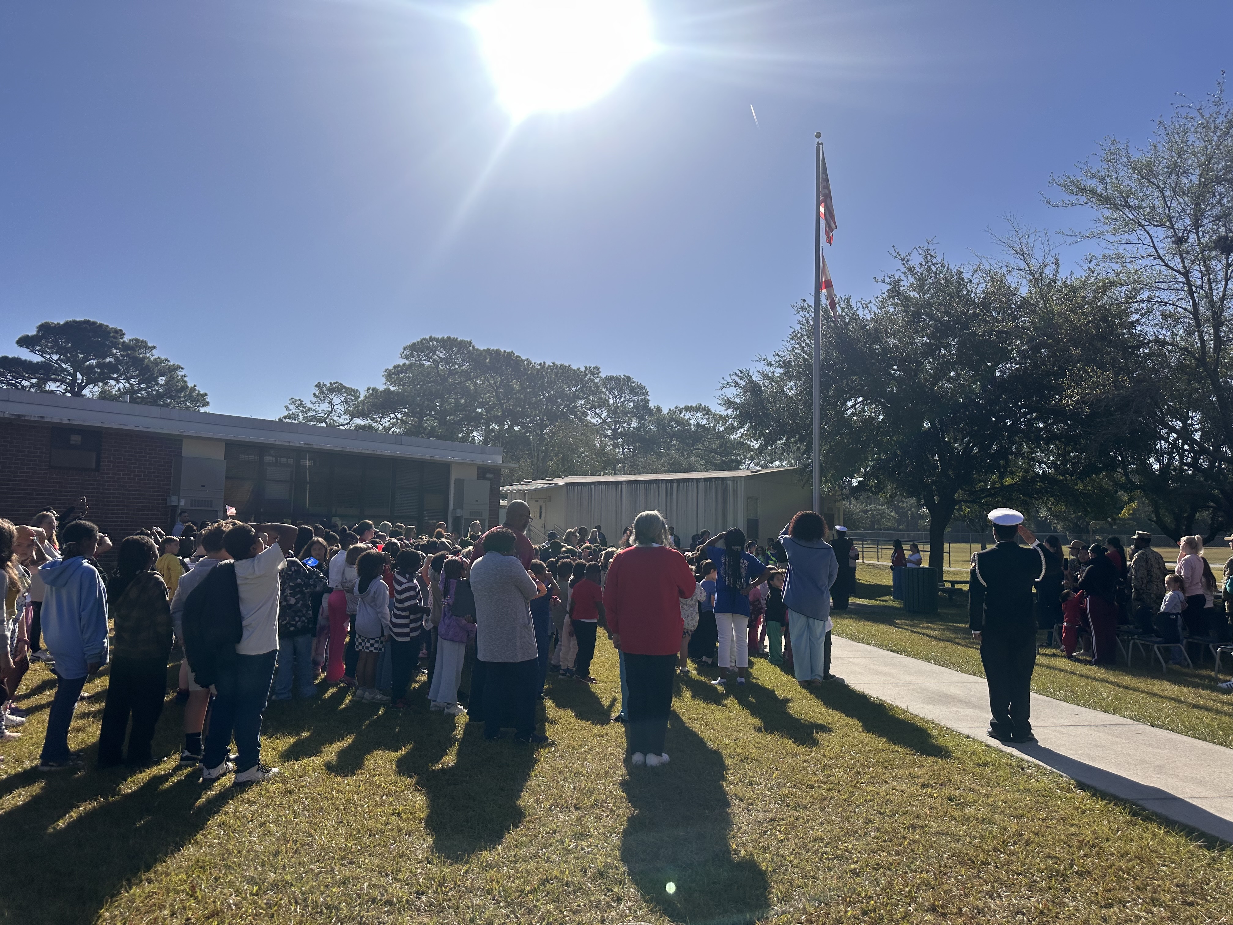 A group of people stand in a line in front of a building on a sunny day.