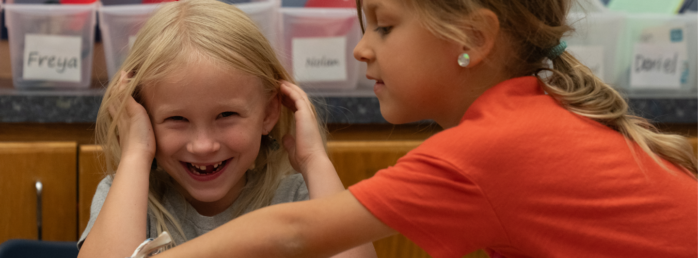 girl laughing while classmate reaches across the table