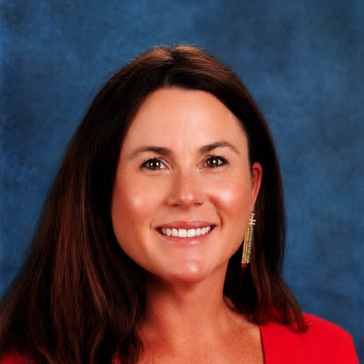 Woman with brown hair, wearing red top, smiling, blue background.