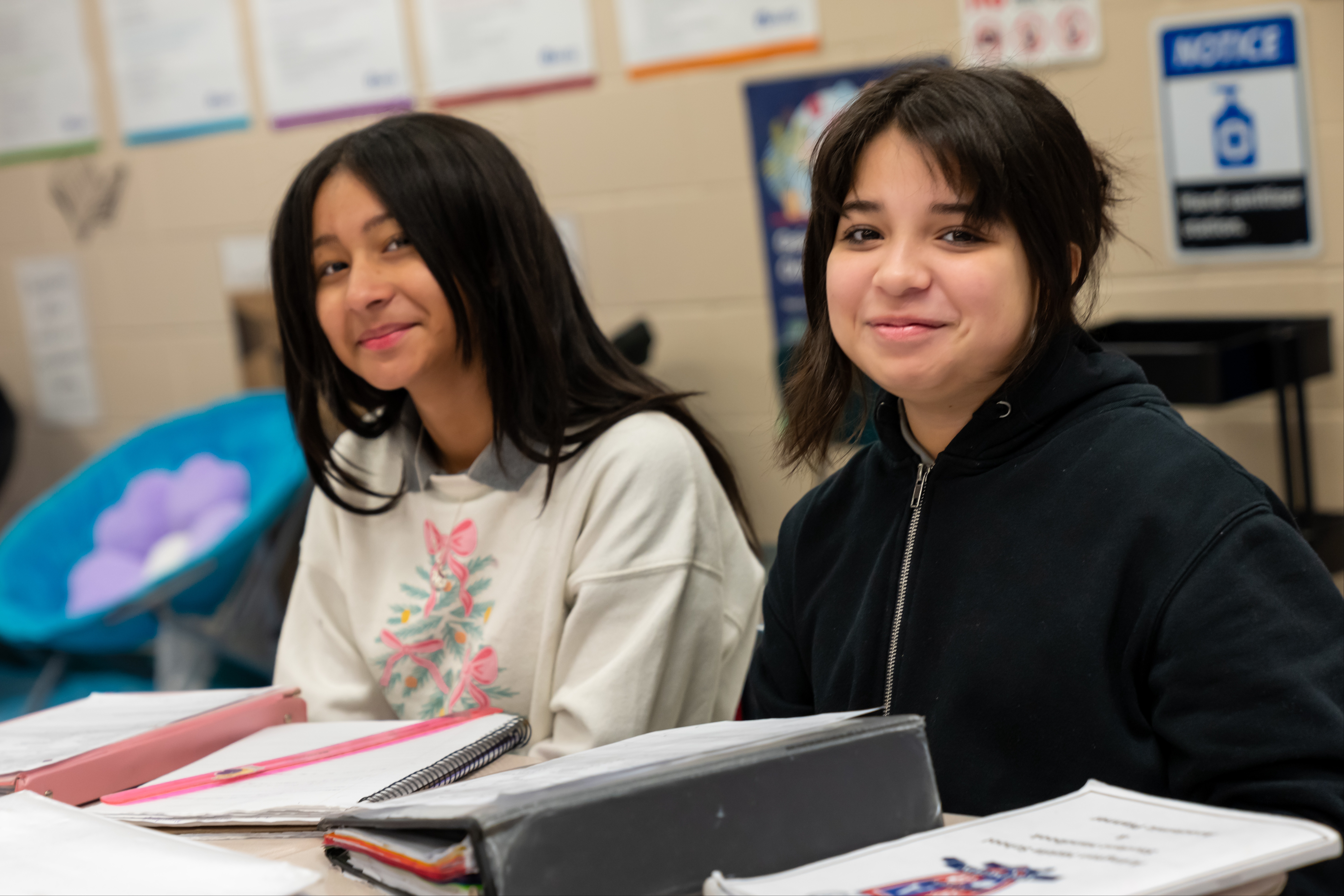 Two female students sitting at their desks with notebooks and paperwork in front of them.