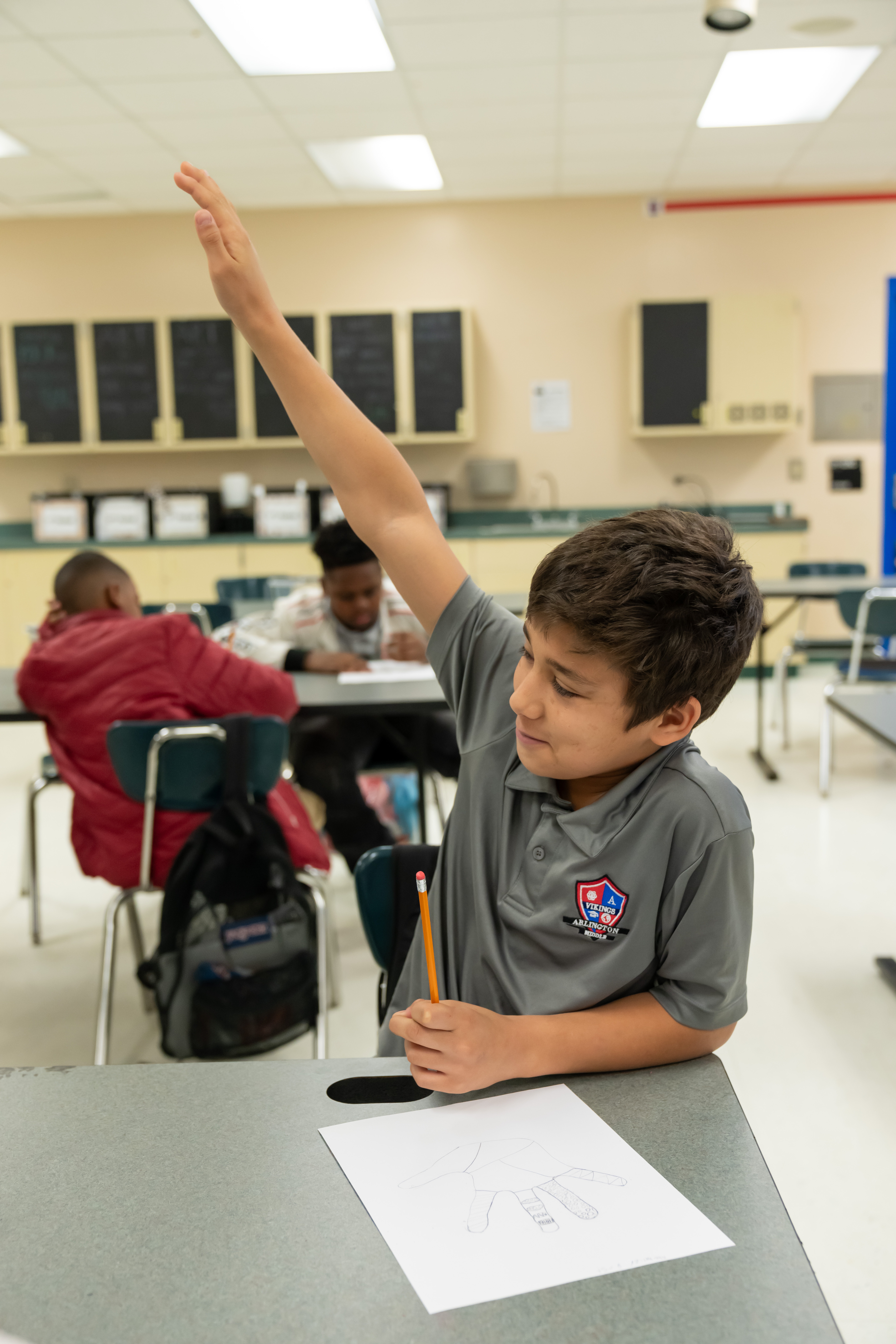Boy in a grey collared shirt with his right hand raised.