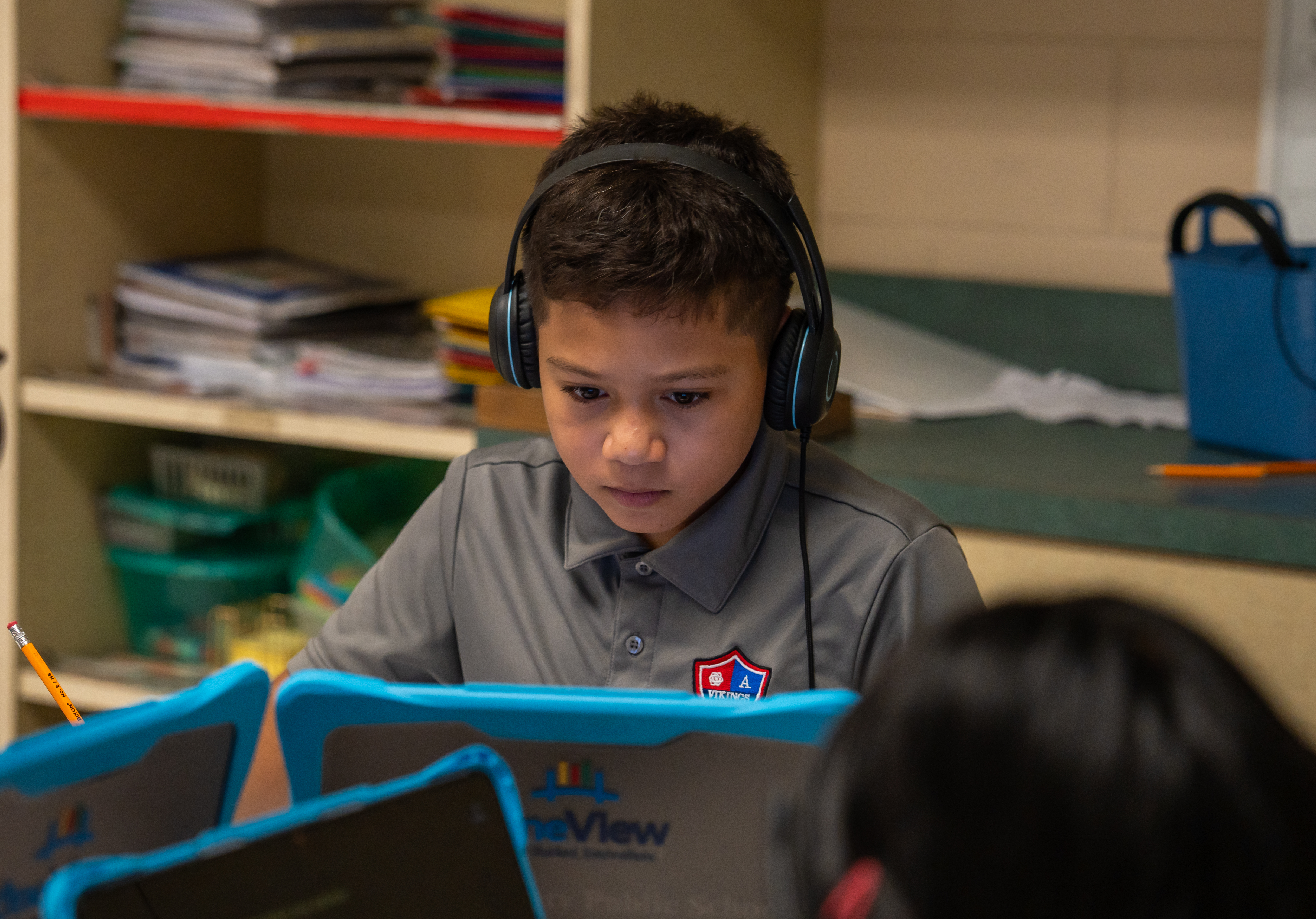 Male student in a gray colored shirt wearing headphones with a computer.