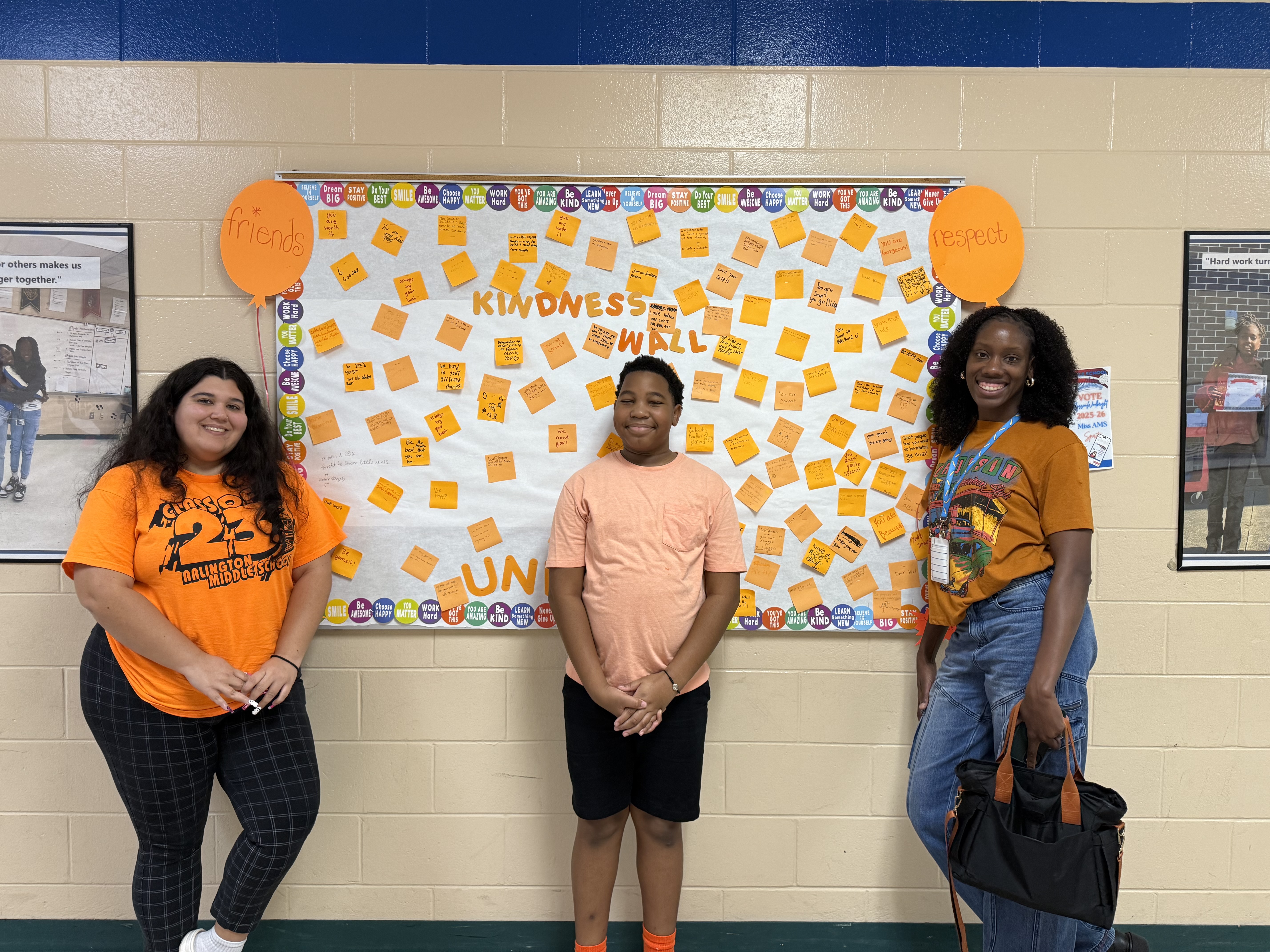Two teachers and a student standing in front of a orange bulletin board.