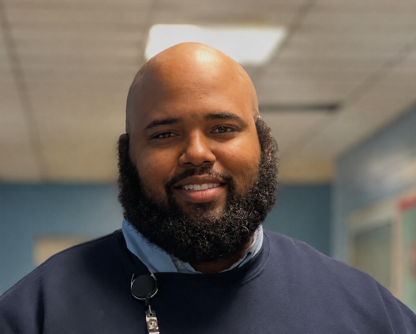 A person wearing a navy blue sweater, a blue collared shirt, and a black lanyard with a badge.
