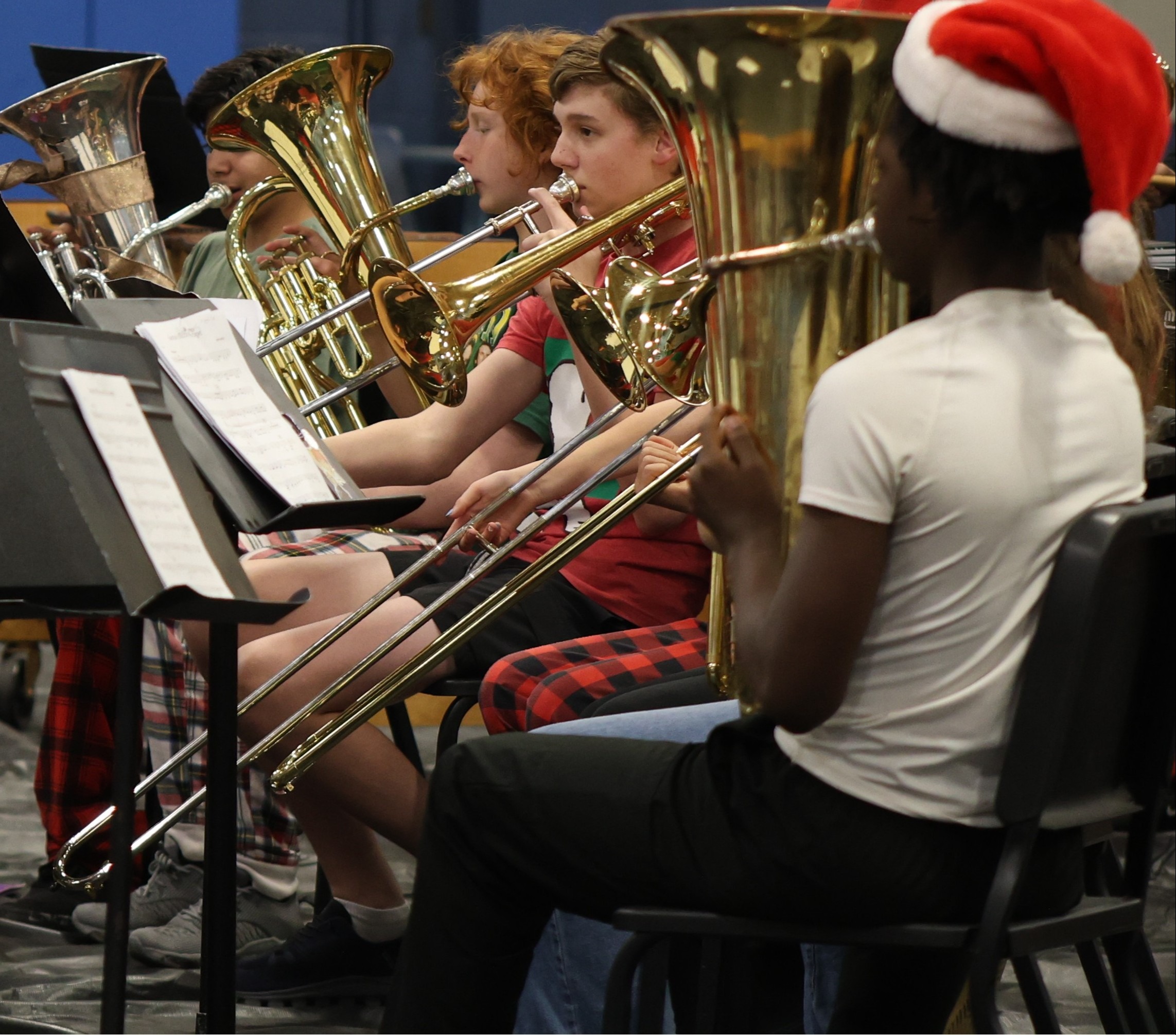 A music ensemble playing brass instruments. A person wears a Santa hat. Several people in red and white checked shirts.