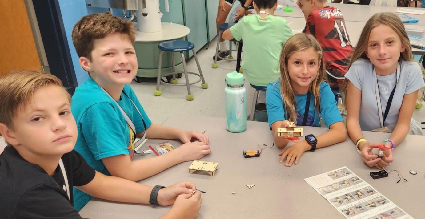 Four children seated at a table with small items and a worksheet in front of them.
