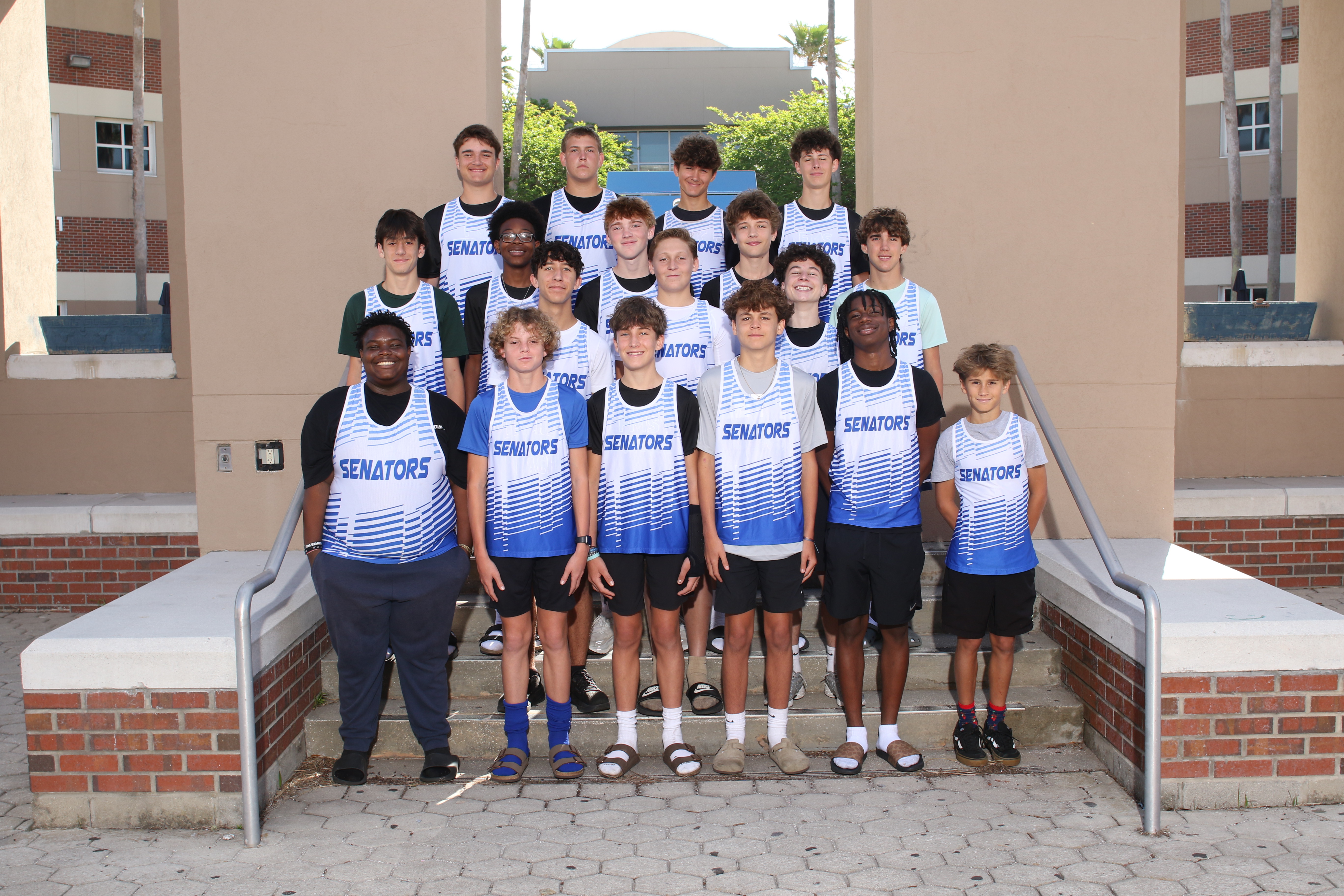A group of young athletes in white and blue jerseys standing on steps in front of a building.