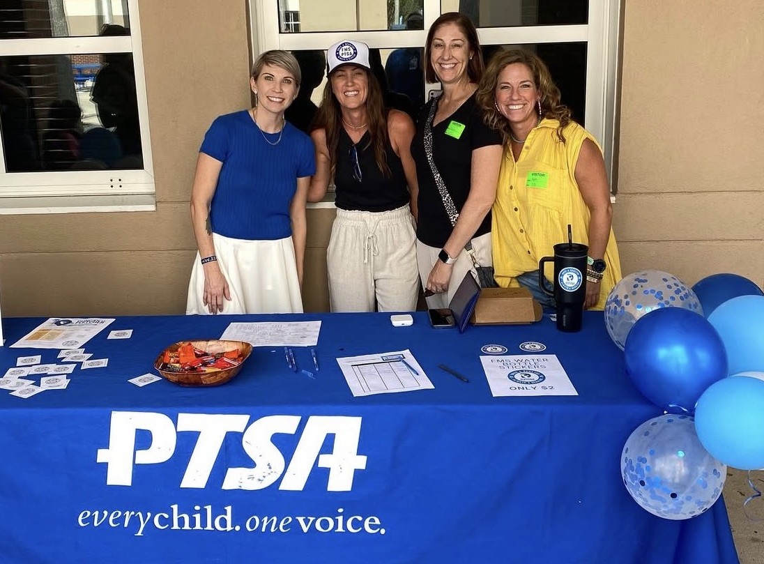 Five women stand behind a blue table with the words "PTSA" and "every child. one voice." A blue banner and balloons.